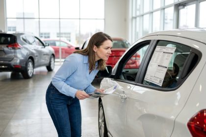 Femme examinant le prix d'une voiture neuve dans une concession automobile moderne en 2026